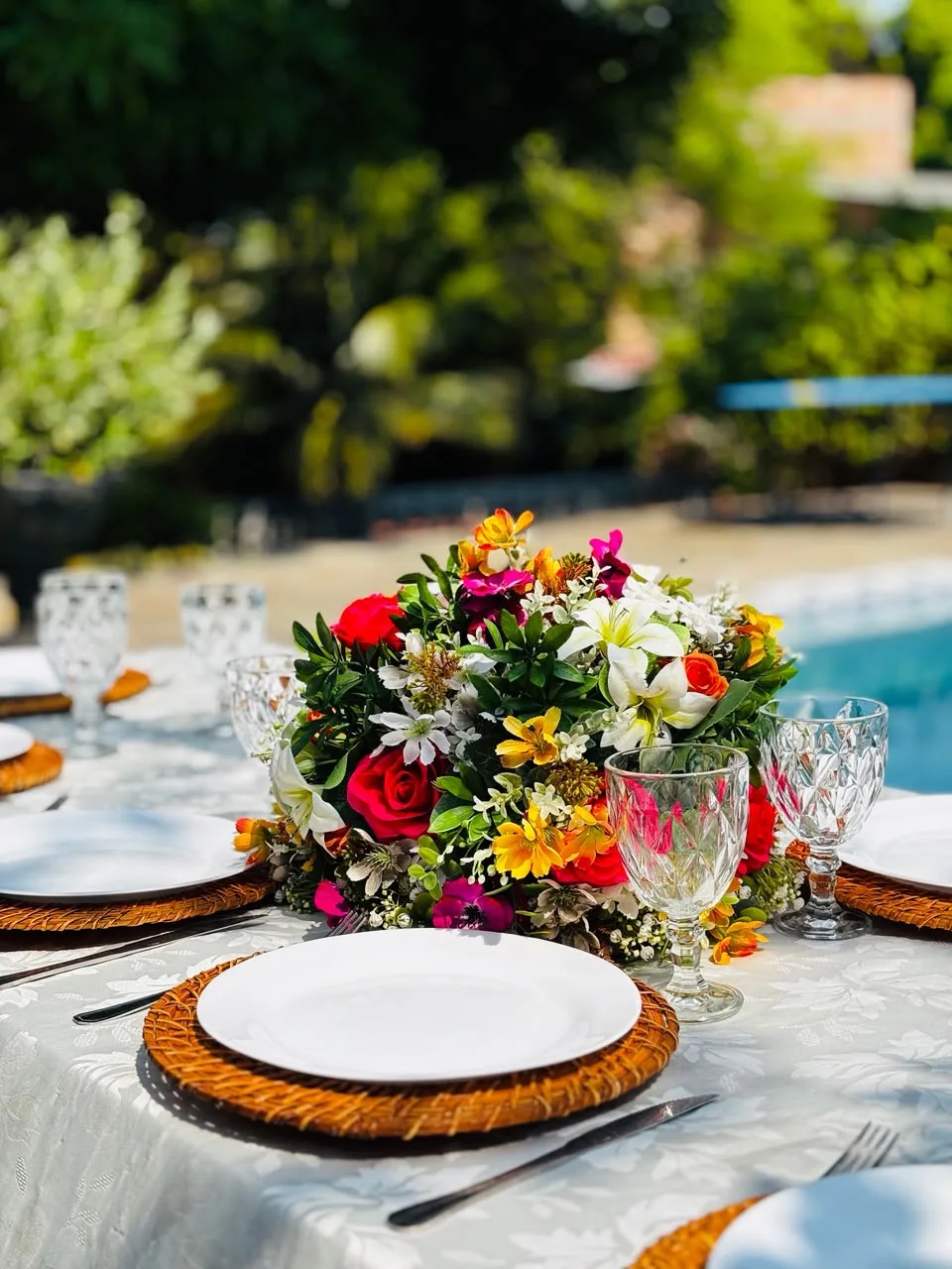 Mesa posta com arranjo colorido de flores ao lado da piscina